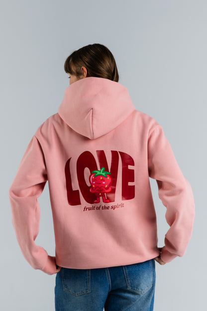 Person wearing a pink hoodie with a red graphic and text on the back, standing against a light gray background#color_pink