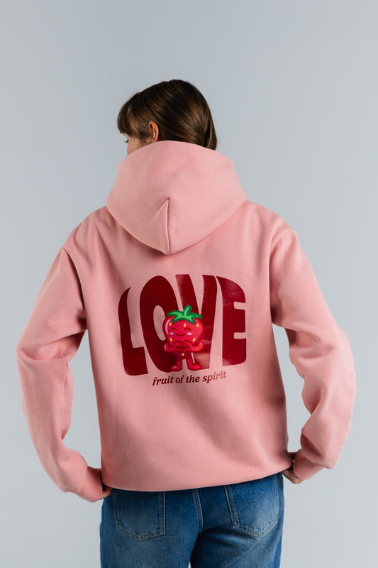 Person wearing a pink hoodie with a red graphic and text on the back, standing against a light gray background#color_pink