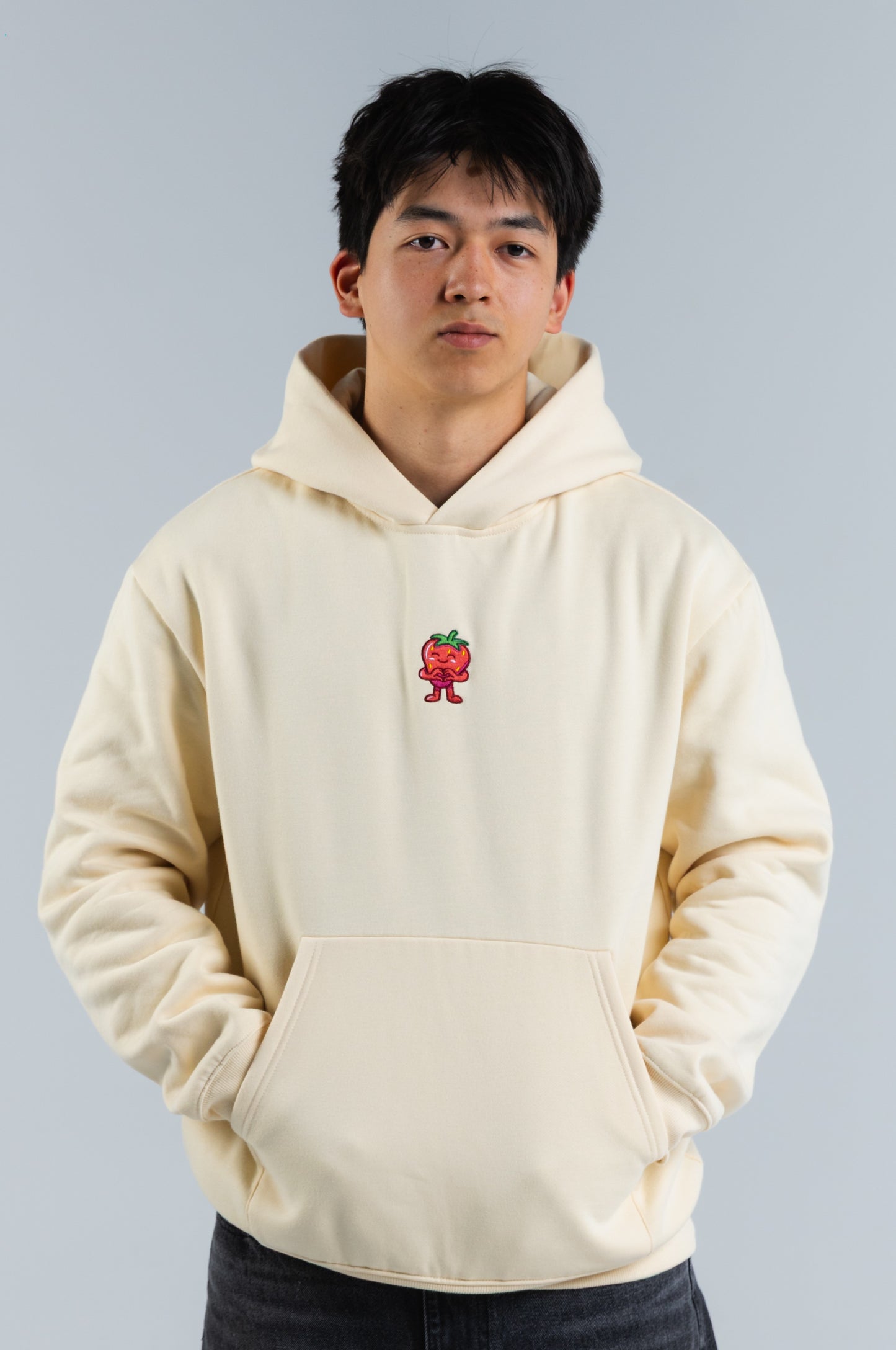 Person wearing a cream hoodie with a small red and green graphic on a plain background#color_cream