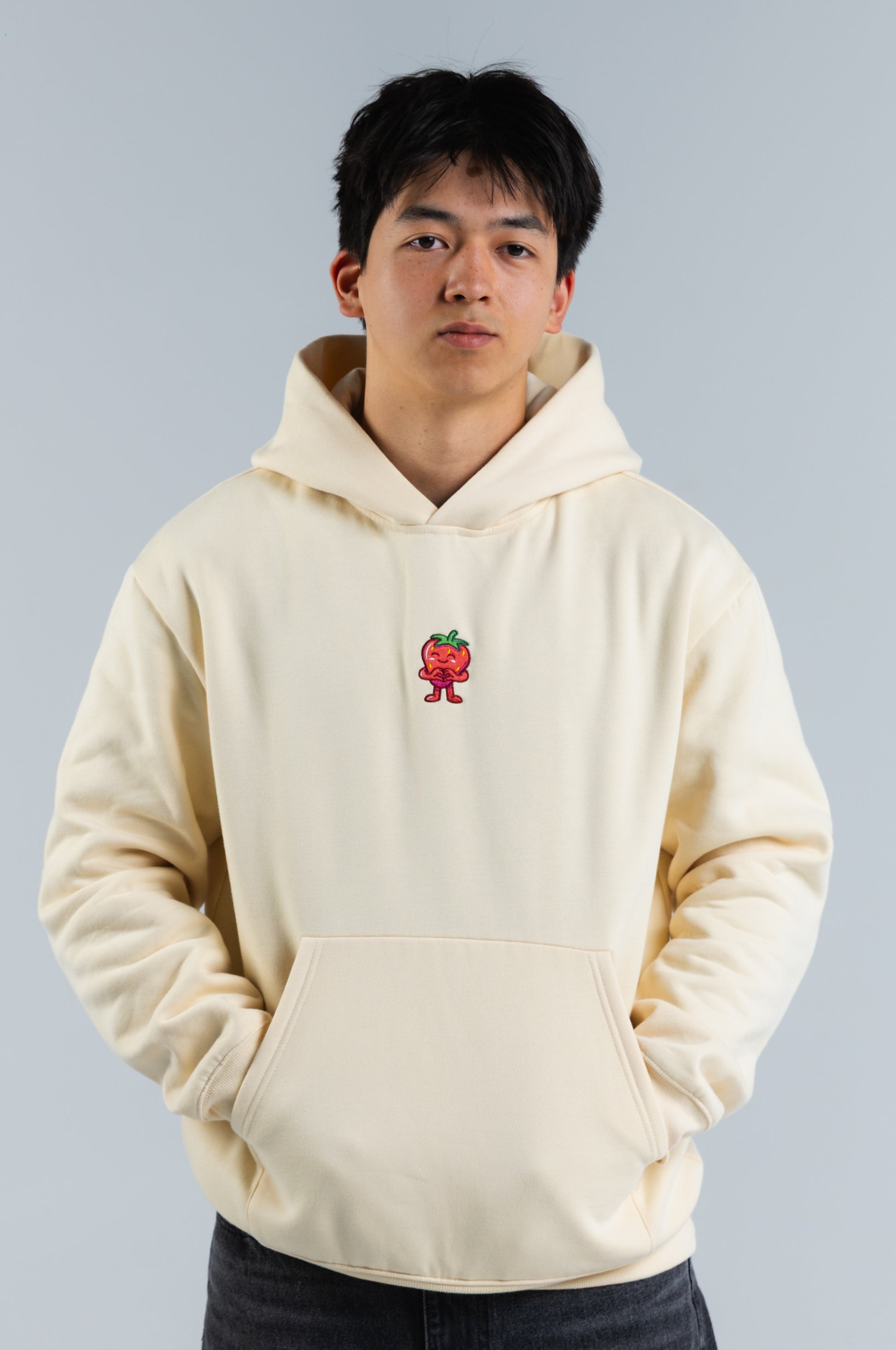 Person wearing a cream hoodie with a small red and green graphic on a plain background#color_cream