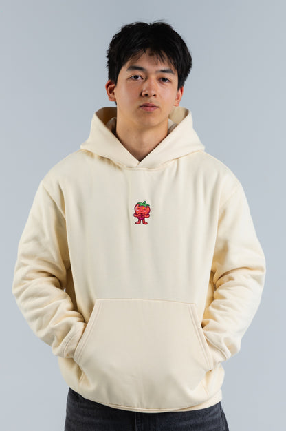 Person wearing a cream hoodie with a small red and green graphic on a plain background#color_cream