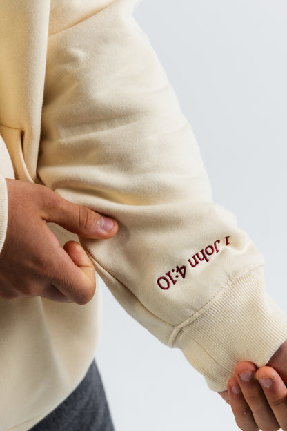 Cream hoodie sleeve with embroidered text held by a person against a light background#color_cream