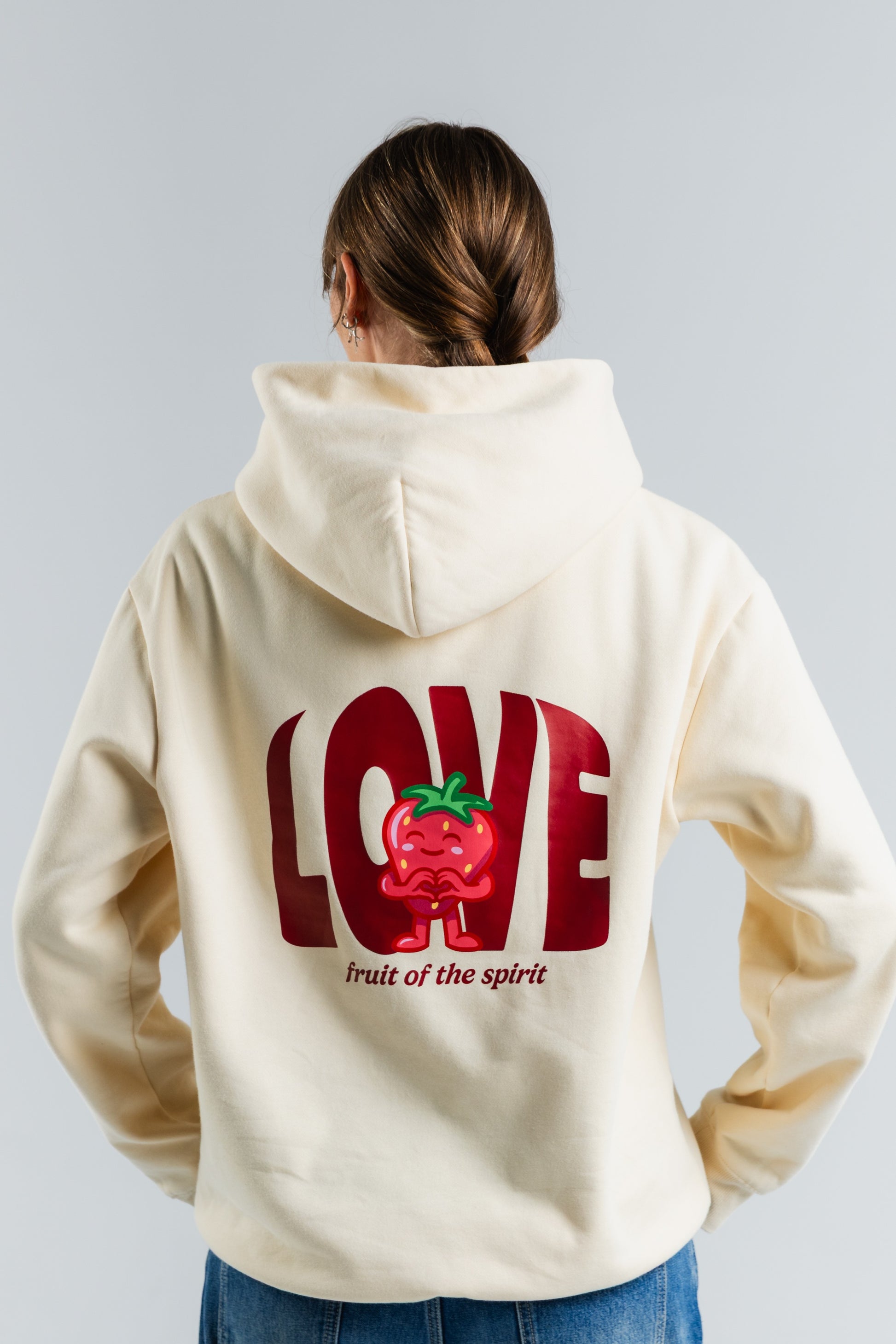 Person wearing a cream hoodie with a red 'LOVE' graphic and text on the back against a light gray background#color_cream