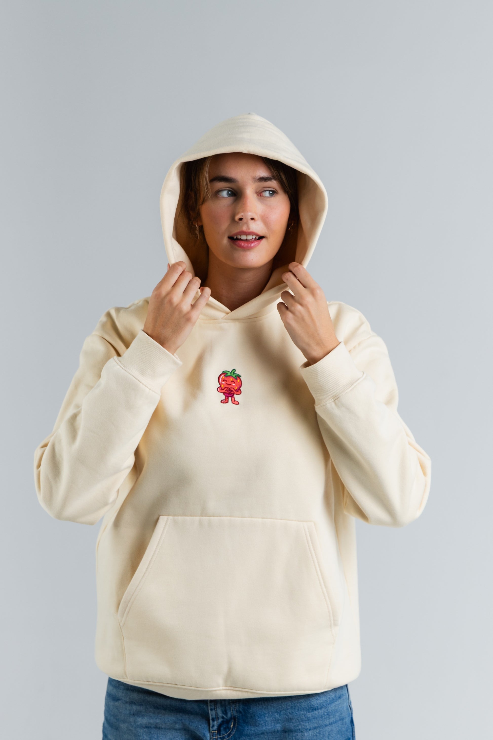 Person wearing a cream hoodie with a small red and yellow graphic on a plain background#color_cream